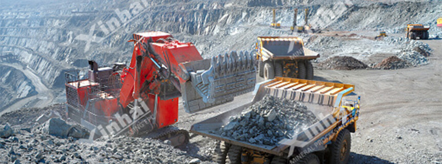 There is an excavator working and dump truck transporting ores to the mine pile on the surface mine.